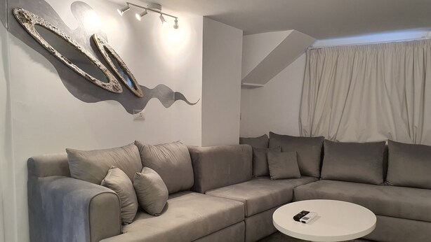 A modern living room with a sectional sofa, a round coffee table, and a decorative wall piece. - AB N401 Spacious 2BR Duplex with Partial Nile View (Giza Governorate)