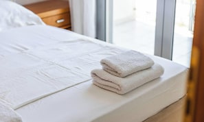 Ein ordentlich bezogenes Bett mit weißen Leinen und einem Stapel gefalteter Handtücher daneben.