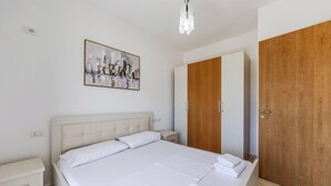 A bedroom with a bed, a nightstand, a wooden wardrobe, and a painting on the wall. - Orikum Beachside Retreat Apartment 2 (Orikum)