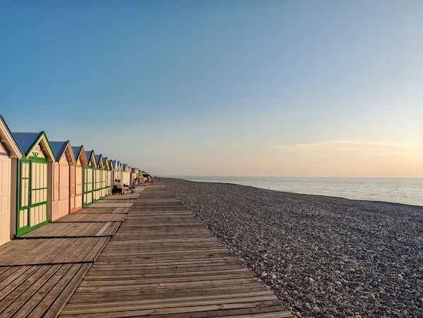 A wooden boardwalk leading to beach huts with a pebble beach.