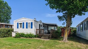 En hvid campingvogn med blå skodder, en veranda og en lille have.