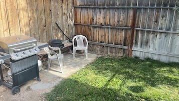 A backyard with a grill, a barbecue, and a chair.