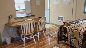A room with a wooden desk, two white chairs, a television, a ceiling fan, a bed with a patterned blanket, and a window with blinds. - Stan's Hideaway in Tropic 9 miles to Bryce Canyon, Tucked away & private, Unique (Tropic)