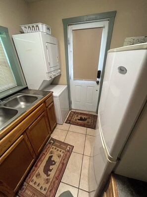A compact kitchen with a sink, wooden cabinets, a white refrigerator, and a door with a window.