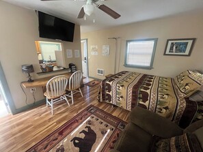 A room with a bed, two chairs, a desk with a computer, a TV, and a window with blinds.