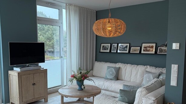 A living room with a sofa, a coffee table, a TV on a cabinet, and a wicker ceiling light fixture. - Where Design Meets Coziness—High-Quality Vacation Rental 5 Minutes from the Beach, 3 Beds (Karlshagen)