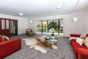 A spacious living room with a glass coffee table, red sofas, and a large window offering a view of the outdoors.
