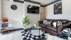 Un soggiorno moderno con un divano in pelle marrone, un tavolino rotondo, una TV a schermo piatto e un elemento decorativo a parete.