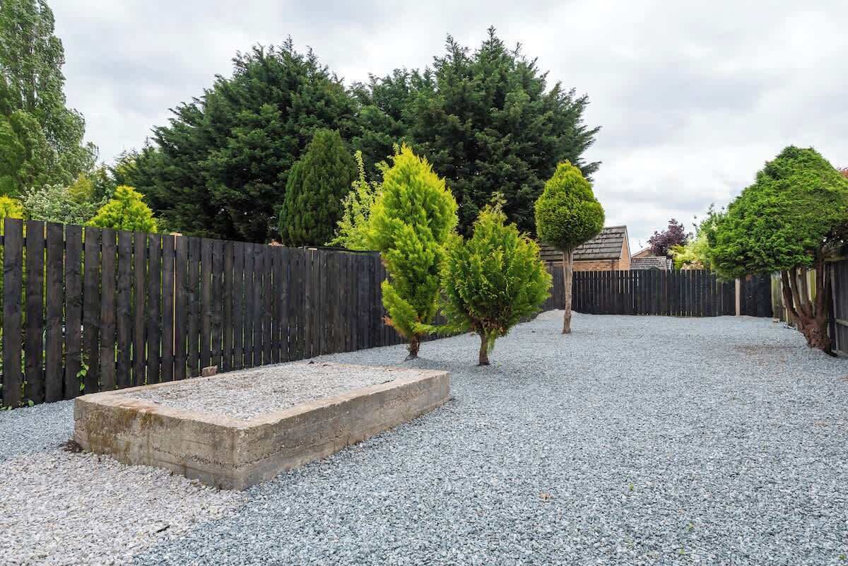 Un sendero de grava que conduce a una valla de madera con un banco de piedra.