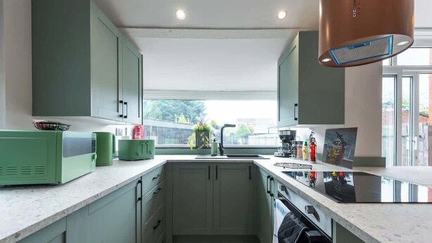 Una cucina moderna con mobili verde chiaro, una cappa aspirante in acciaio inossidabile e un'ampia finestra che offre luce naturale.