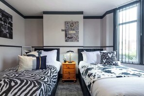 Habitación de hotel con dos camas, una mesita de noche, una lámpara y una obra de arte en la pared.