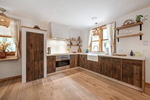 Moderni keittiö, jossa on puukalusteet, sisäänrakennettu uuni ja ikkuna, jossa on verhot.