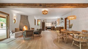 Uma sala de estar espaçosa com teto de madeira, uma mesa de jantar com cadeiras e uma cozinha ao fundo.