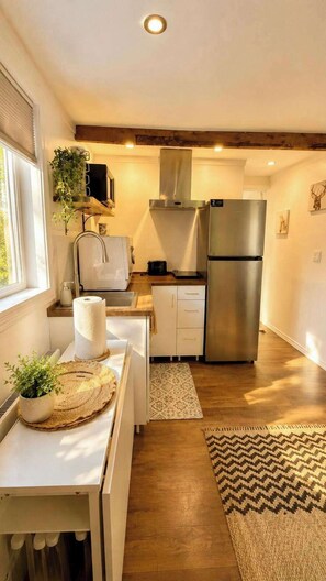 A kitchen with a stainless steel refrigerator, a microwave, a sink, and a wooden ceiling.