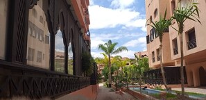 Ein Innenhof mit Pool, Palmen und Gebäuden mit Bogenfenstern und Balkonen.
