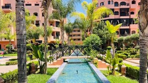 A pool surrounded by lush greenery and multi-story buildings with balconies. - Nice Property Marrakech Village With Pools and Gardens (Marrakech)