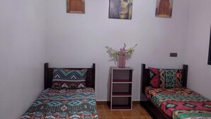A bedroom with two beds, each with patterned bedding, a small shelf unit, and two wall-mounted pictures. - Nice Property Marrakech Village With Pools and Gardens (Marrakech)