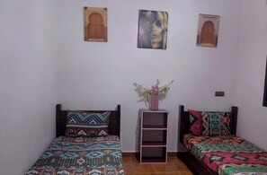 Ein Schlafzimmer mit zwei Betten, beide mit gemusterten Bettbezügen, einer kleinen Regalwand und zwei Wandbildern.