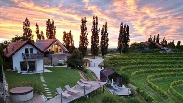 Een modern huis met een terras, een jacuzzi en een wijngaard op de achtergrond.