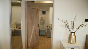 Een hal met een houten deur, een witte console en een vaas, plus een lamp.