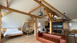 Een slaapkamer in loftstijl met een houten plafond, een bed, een leren bank en een kitchenette.