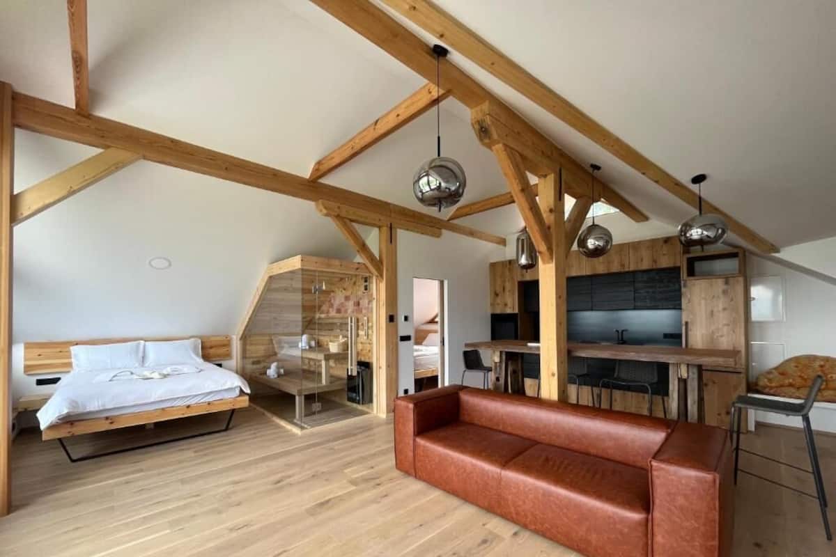 Ett sovrum i loftstil med ett träpanelat tak, en säng, en soffa i läder och ett litet kök.