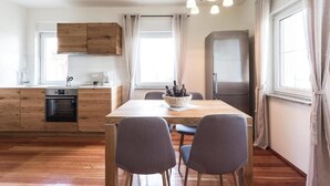 Een moderne keuken met houten kastjes, een inbouwoven, een eettafel met stoelen en een koelkast.