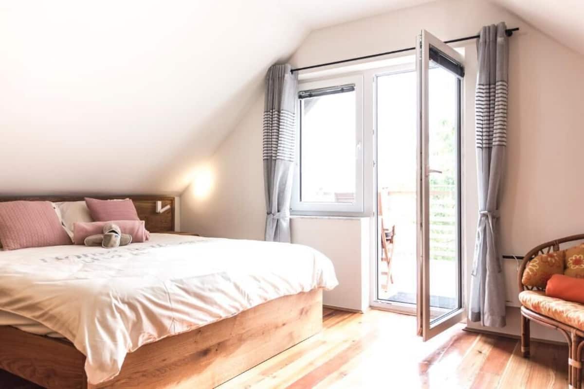 A bedroom with a wooden bed, a sofa, a window with curtains, and a view of the outdoors.