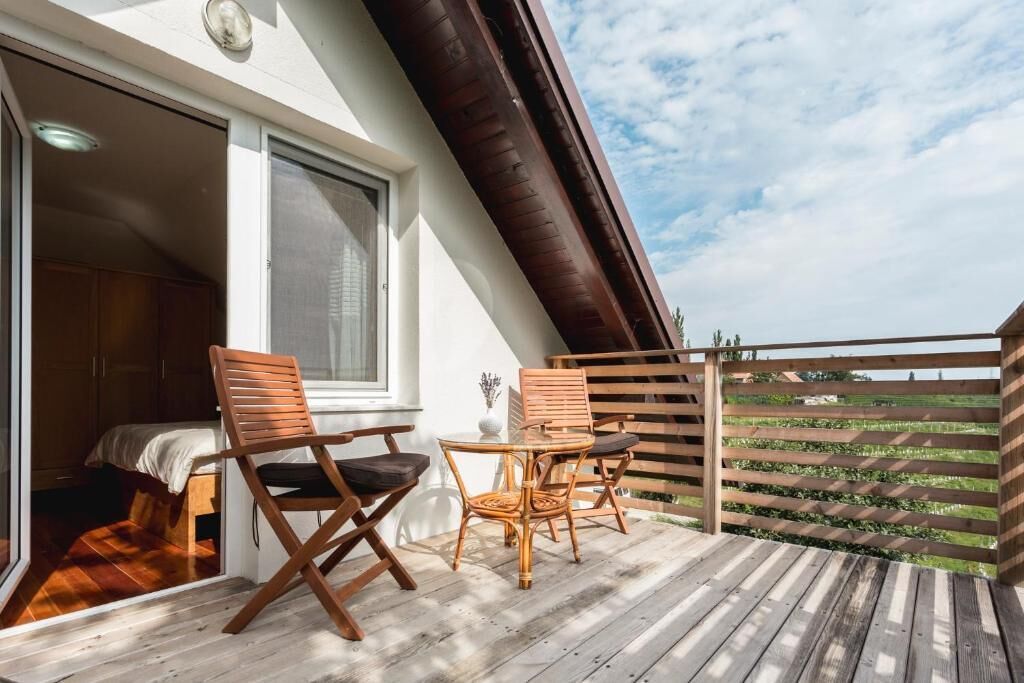 A balcony with wooden chairs and a table, a window, and a view of a green landscape.