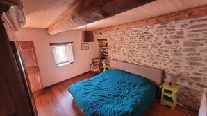 Une chambre avec un lit, une fenêtre, un mur en pierre et un plafond en bois.