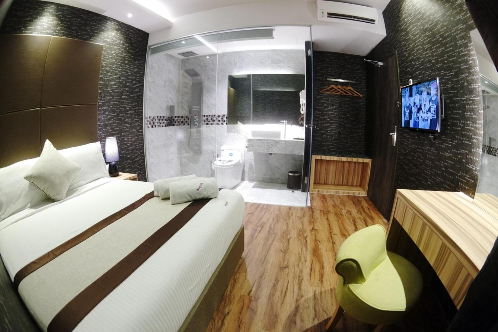A modern hotel room with a large bed, a small seating area, a shower, and a television.