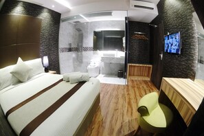 A modern hotel room with a large bed, a small seating area, a shower, and a television. - Herehotel.com (Johor Bahru)