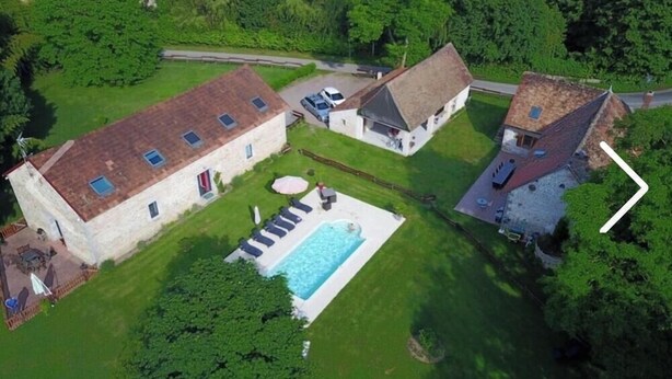 Vista aérea de una propiedad con piscina, edificios de piedra y patio cercado.