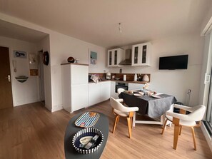 Eine moderne Küche mit weißen Schränken, einem Essbereich mit Tisch für vier Personen und einem an der Wand montierten Fernseher.