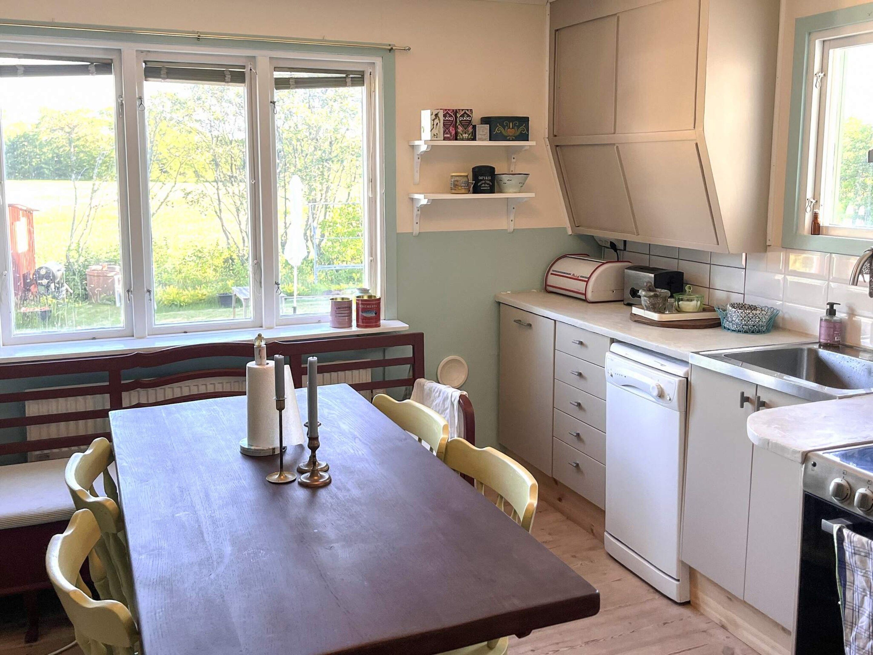 Une cuisine équipée d’une table à manger, de chaises, d’un lave-vaisselle et d’une fenêtre donnant sur un espace verdoyant.