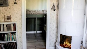 A room with a fireplace, a bookshelf, a door leading to a loft, and a wall-mounted light fixture. - 4 Person Holiday Home in Ronneby (Listerby)