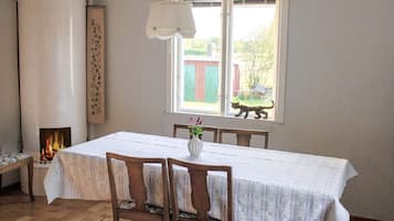 Un comedor con una mesa dispuesta para cuatro, sillas de madera, un florero con flores, una lámpara colgante y una ventana con vistas al exterior.