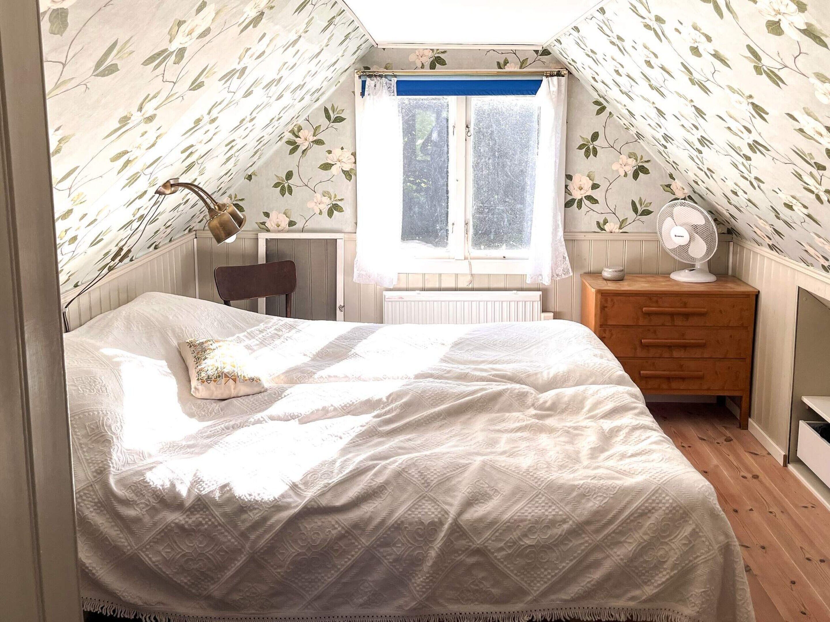 A bedroom with a bed, a chair, a dresser, a window, and a radiator.