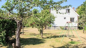 A residential property with a large tree, a swing set, and a white building with a metal roof. - 4 Person Holiday Home in Ronneby (Listerby)
