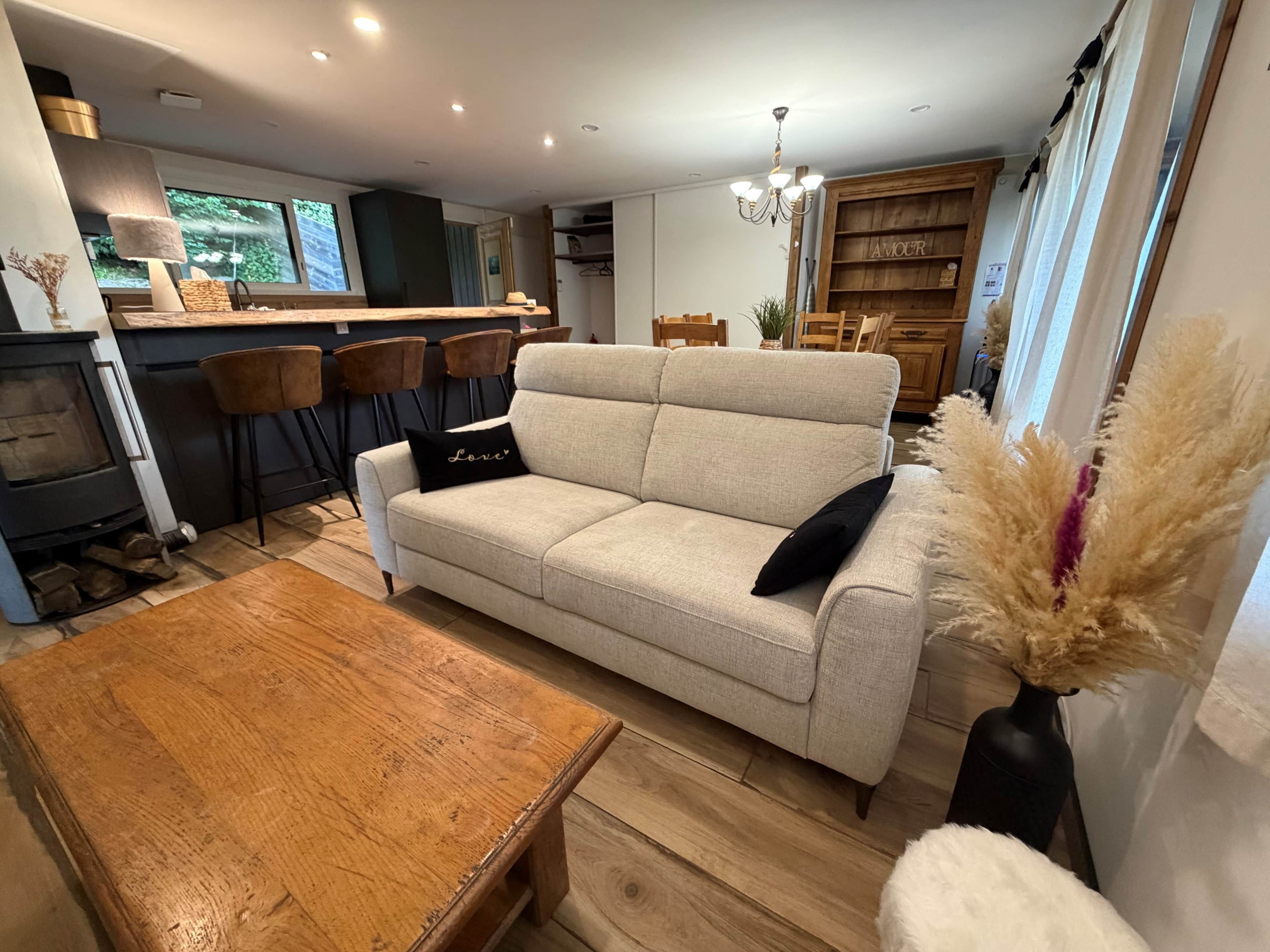 A living room with a sofa, a wooden coffee table, a fireplace, and a kitchen area in the background.