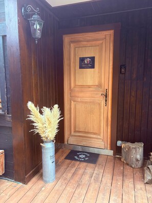 Eine Holztür mit einem Schild, ein Metalllaterne, ein Metallkübel mit Pampasgras und eine Holzbank.