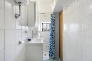 Un baño con paredes de azulejos blancos, un lavabo, un espejo y una cortina de ducha.