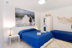 A room with a bed, a small table, a cabinet, and a wall-mounted picture of a lighthouse.