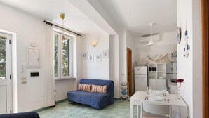 Una habitación con sofá, una mesa de comedor con sillas, una pequeña cocina y una ventana con cortinas.