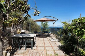 A patio with a table and chairs, a sun umbrella, and a view of the sea.