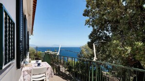 Un balcón con mesa y sillas, con vistas a la costa, árboles y un cielo despejado.