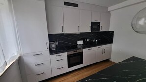 A modern kitchen with white cabinets, a black countertop, and a built-in oven. - Rudolph Apartments Kleve - Apartment 5 (Kleve)