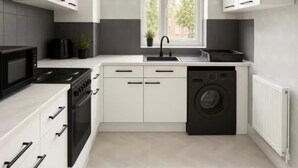 Une cuisine moderne avec des meubles blancs, une cuisinière noire, un four à micro-ondes, un évier et un lave-linge.