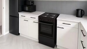 Une cuisine avec des meubles blancs, une cuisinière noire et un four à micro-ondes noir.