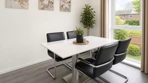 Une salle de réunion moderne avec une table blanche, des chaises noires et trois œuvres d’art florales décorant les murs.
